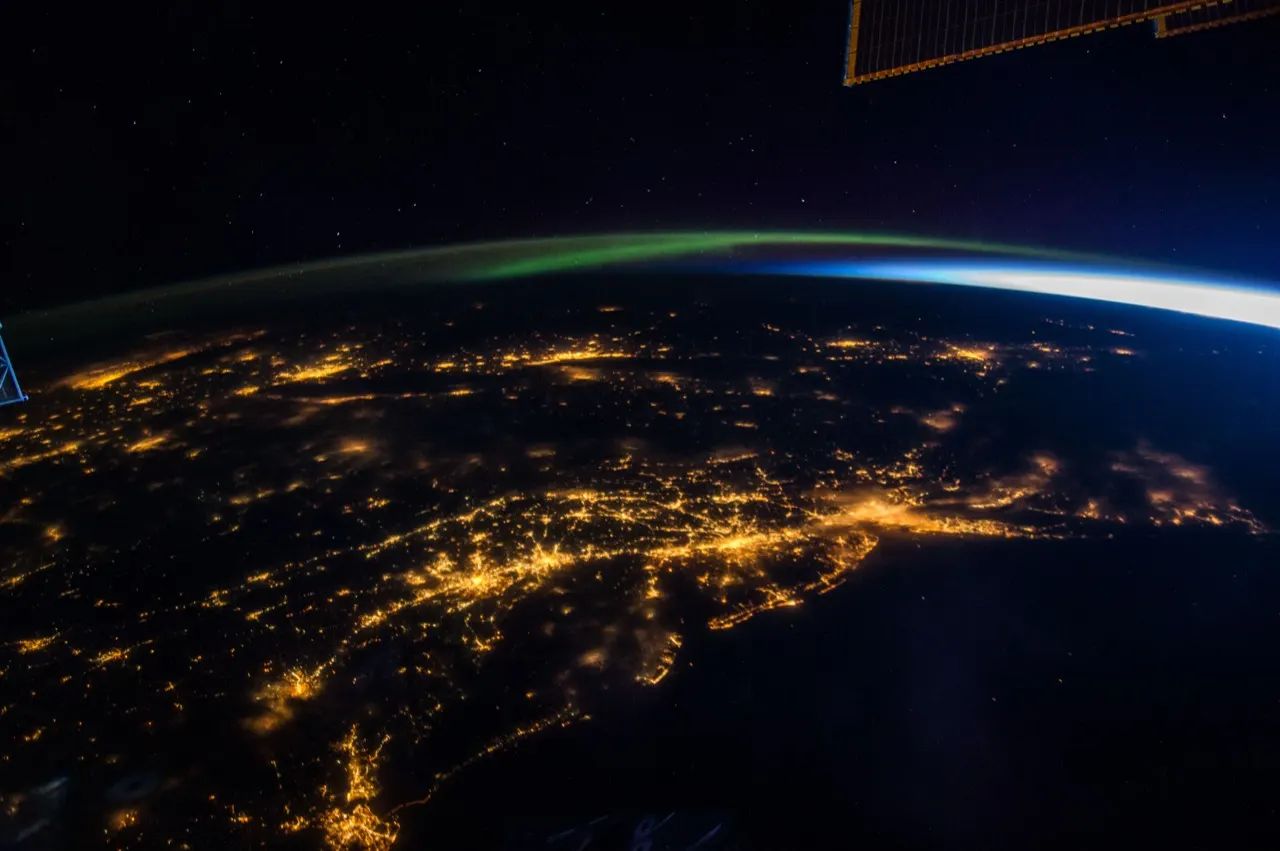 Earth at night from the International Space Station, with city lights and an aurora on the horizon